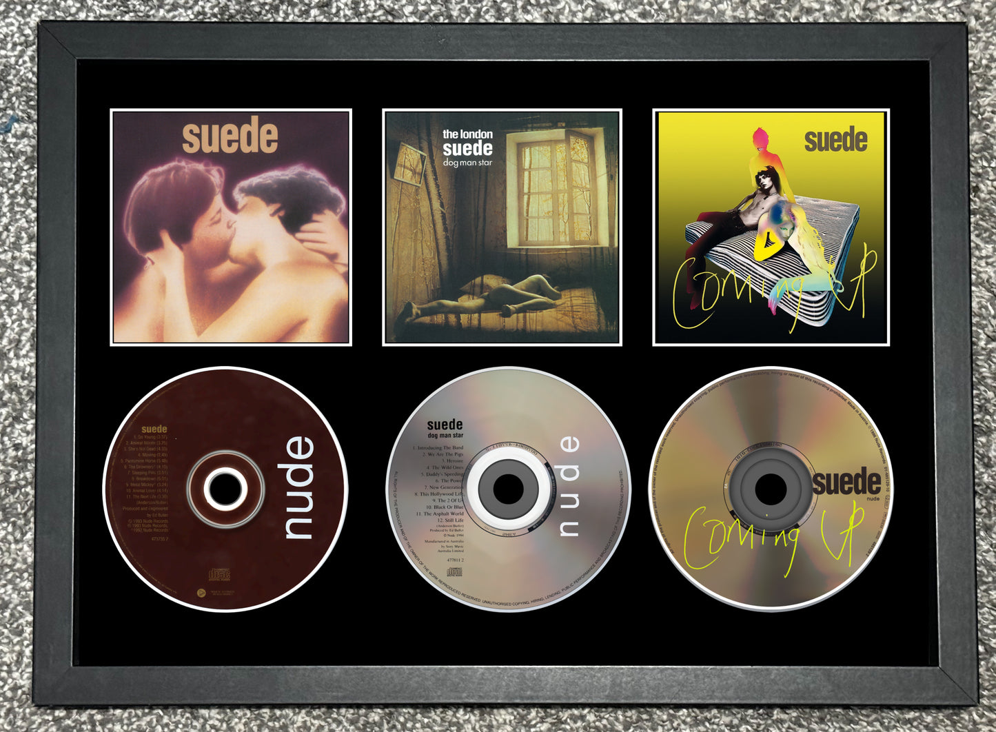 Framed album covers and CDs of the band Suede on a textured gray background