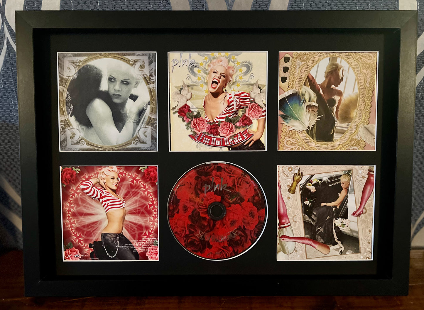 Framed album cover with a central red CD and decorative images on a patterned background
