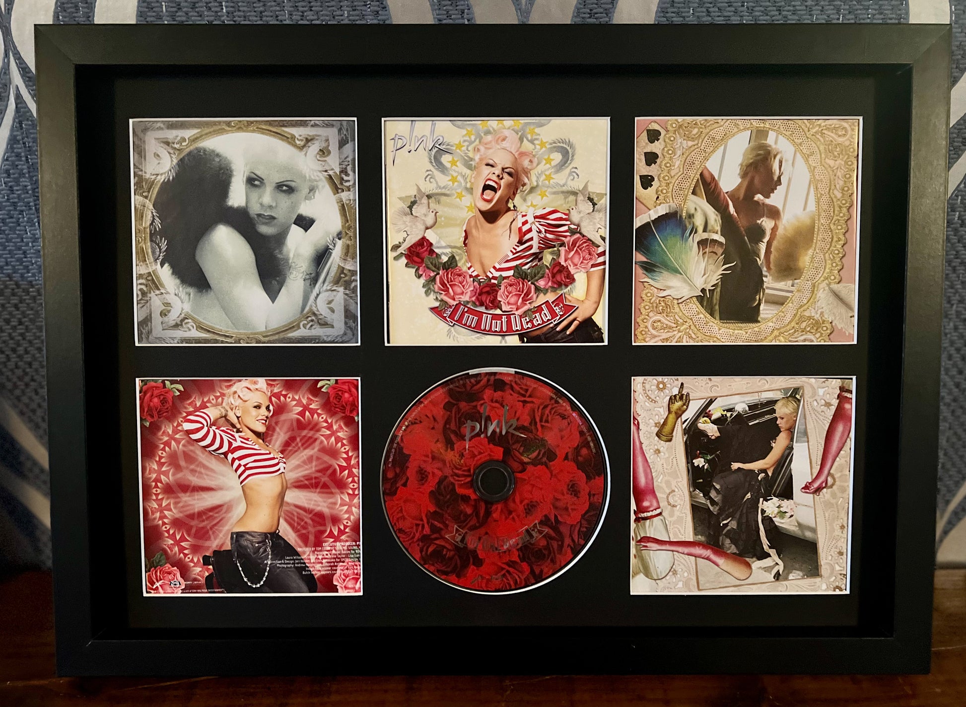 Framed album cover with a central red CD and decorative images on a patterned background