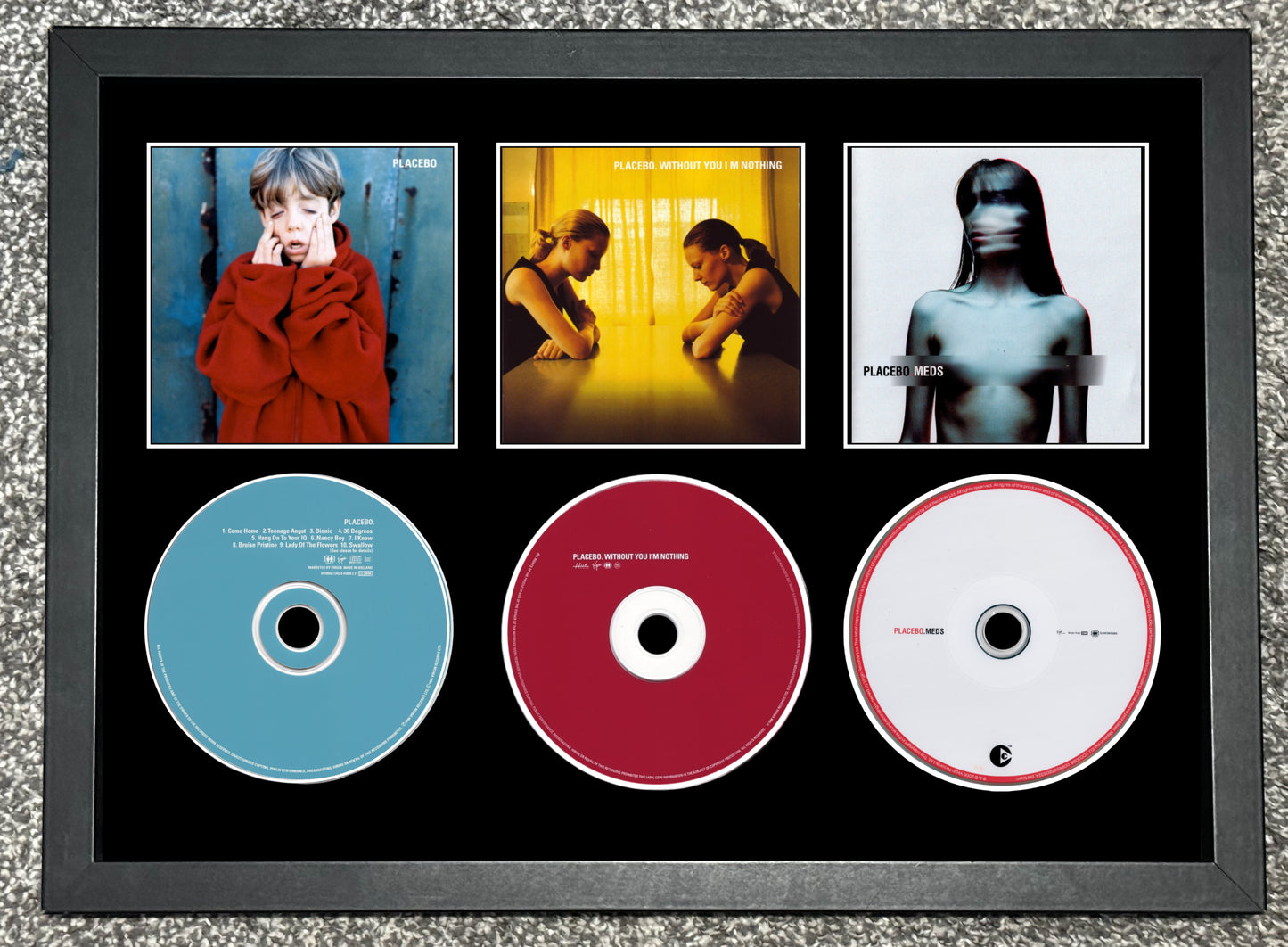 Framed album covers and CDs with a black border on a textured surface